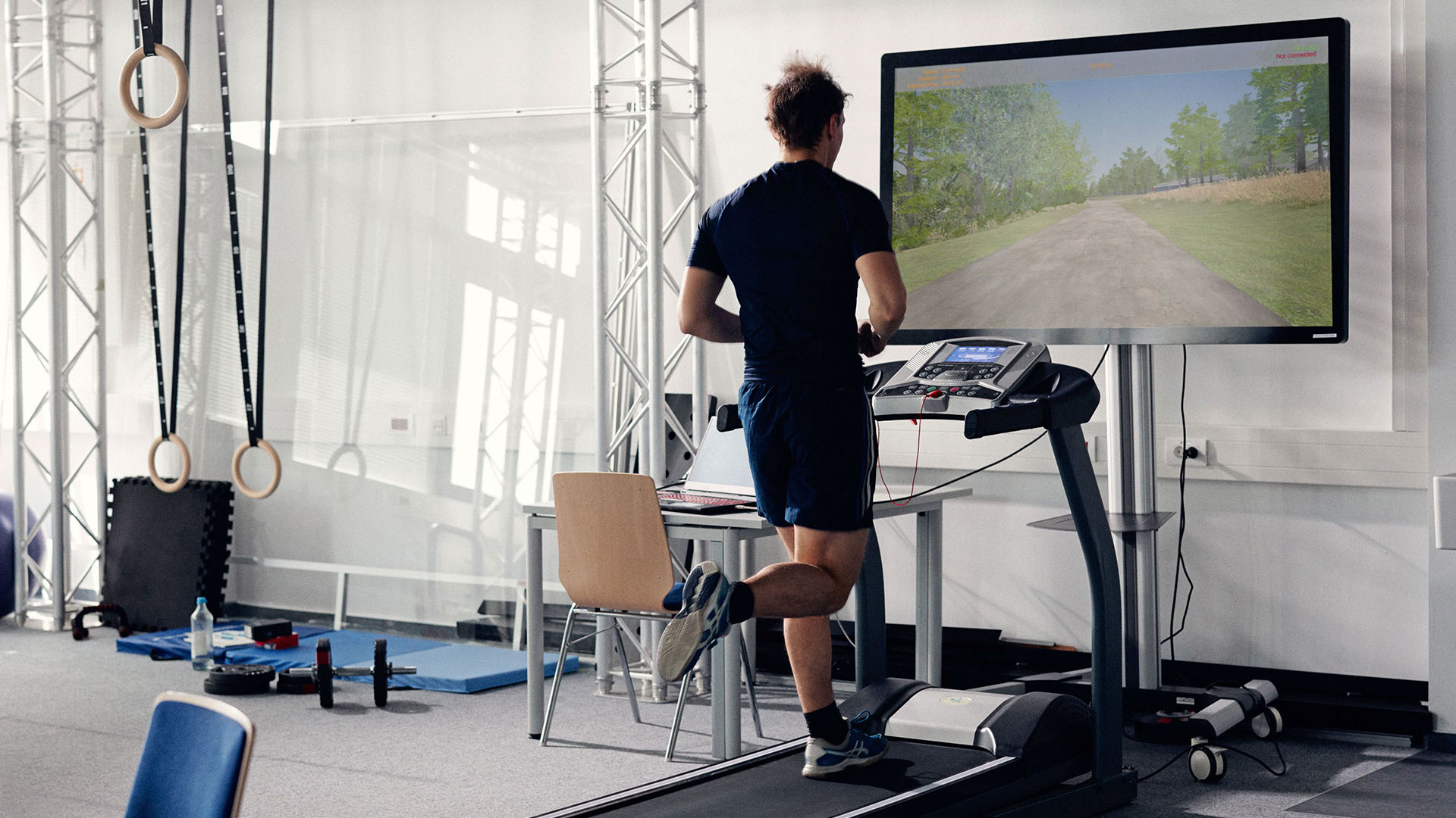 Impression Forschungsprojekt KI-SIGS Bewegungstraining; Mann benutzt Laufband mit virtuellem Trainingssystem